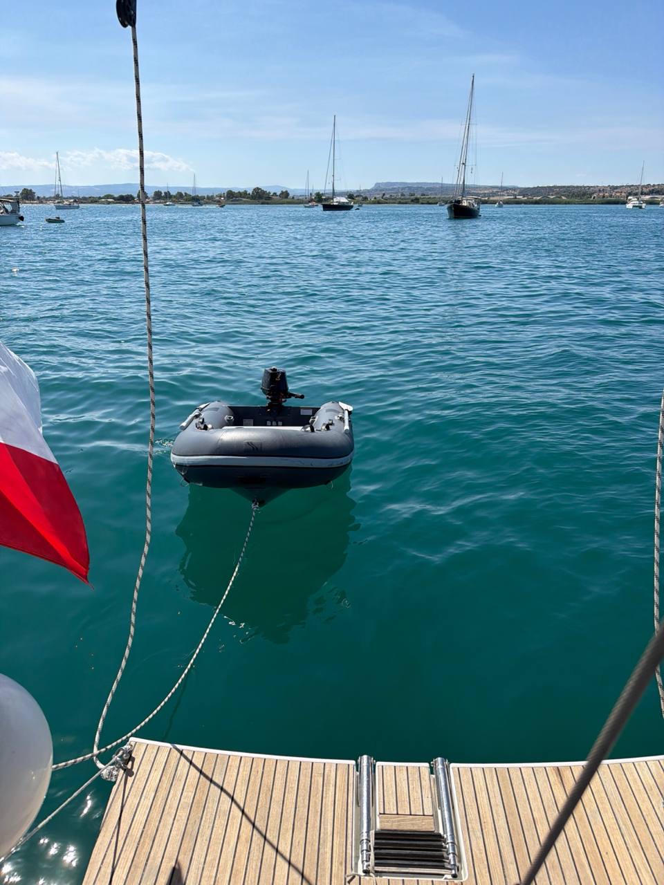 Tender astern of Everything Zen in the clear green water of Porto Grande, Siracusa, with anchored yachts beyond